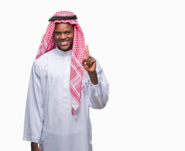 Geleneksel keffiyeh ve parmak gülümseyen süre bir numara ile kendinden emin ve mutlu yukarıyı gösteren izole arka plan üzerinde giyen genç Arapça Afrika adam.