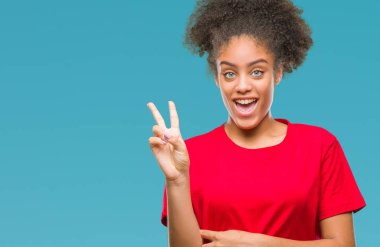 Mutlu yüz zafer işareti yaparken kameraya göz kırpıyor ile gülümseyen izole arka plan üzerinde genç afro Amerikalı kadın. İki numaralı.