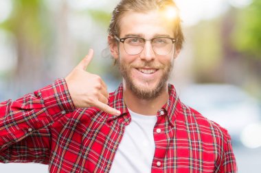 Genç yakışıklı adam uzun saçlı gözlüklü yapıyor gülümseyen izole arka plan üzerinde telefon hareketi ile el ve parmak telefonda konuşuyor gibi. Kavramları iletişim.