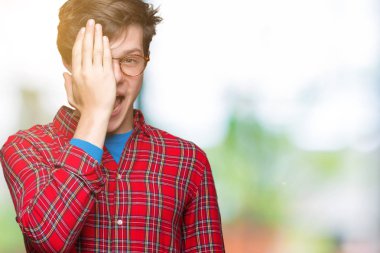 El yüz ve sürpriz duygu kendinden emin gülümseme ile tek gözüyle kapsayan izole arka plan üzerinde gözlük takan genç yakışıklı adam.