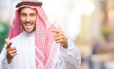 Keffiyeh fotoğraf makinesi ile mutlu ve komik yüz için parmakları işaret izole arka plan üzerinde giyen genç yakışıklı adam. İyi enerji ve vibes.