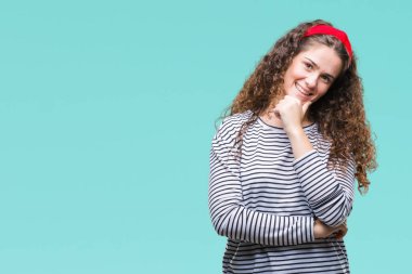 Güzel esmer kıvırcık saçlı Genç kız emin çapraz kollar ve çeneme kaldırdı el ile gülümseme ile kameraya bakarak izole arka plan üzerinde çizgili kazak giyiyor. Pozitif düşünce.