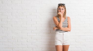 Genç güzel sarışın kadın yüzünden stresli ve gergin ile beyaz duvara çivi ısırma dudaklarından eller. Anksiyete sorunu.