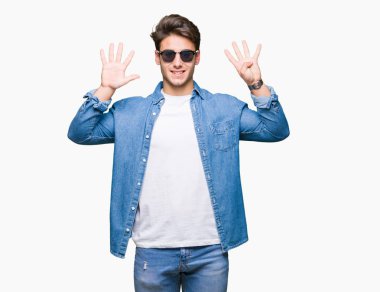 Yakışıklı delikanlı üzerinde güneş gözlüğü takıyor gösterilen arka plan izole ve parmakları ile işaret numara 9 kendinden emin ve mutlu gülümseyerek süre.
