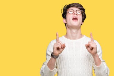 Yakışıklı delikanlı hayrete ve yukarıya bakıyor ve parmakları ile işaret ve silah kaldırdı sürpriz izole arka plan üzerinde gözlük.