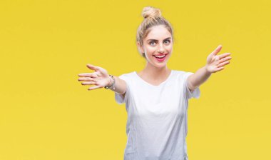 Sarılmak için kollarını açarak gülümseyerek kameraya bakarak izole arka plan üzerinde beyaz t-shirt giyen genç güzel sarışın bir kadın. Neşeli ifade kucaklayan mutluluk.