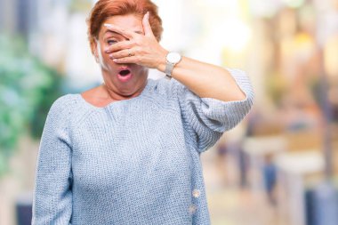 Mahcup ifadeyle parmaklarımın arasından seyir yüz ve gözler el ile kapsayan şok izole arka plan bakmak üzerinde kış kazak giyen Atrractive üst düzey beyaz Kızıl saçlı kadın.