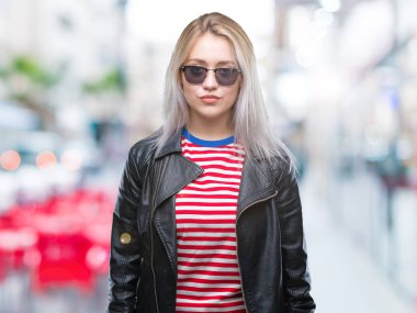 Sarışın genç kadın yüzünde ciddi bir ifade ile izole arka plan üzerinde moda ceket ve güneş gözlüğü takıyor. Basit ve doğal kameraya bakıyor.