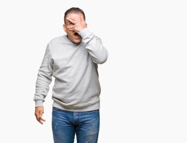 Mahcup ifadeyle parmaklarımın arasından görünen yüz ve gözler el ile kapsayan şok izole arka plan bakmak üzerinde spor kazak giyen orta yaş Arap adam.