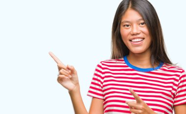 Asyalı genç bir kadın izole edilmiş arka planda gülümsüyor ve kameraya bakıyor iki eliyle ve parmaklarıyla kenarı işaret ediyor..
