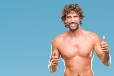 Yakışıklı İspanyol modeli adam seksi ve gömleksiz izole arka plan başarı işareti el ile pozitif jest yapıyor üzerinde başparmak gülümseyen ve mutlu. Neşeli bir ifadeyle, kazanan jest kameraya bakıyor.