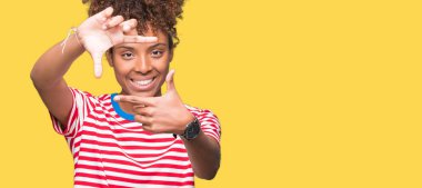 Güzel genç Afro-Amerikan kadın elle yapma çerçeve ve parmakları ile mutlu yüz gülümseyen izole arka plan yüzünden. Yaratıcılık ve Fotoğrafçılık kavramı.