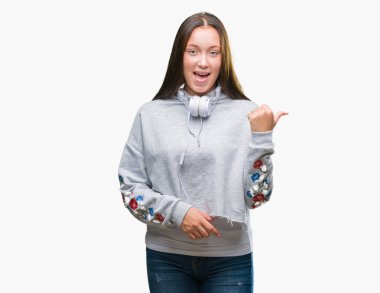 Seyir ve başparmak yanında yukarıyı mutlu yüz ile gülümseyen izole arka plan üzerinde kulaklık giyen genç güzel beyaz öğrenci kadın.