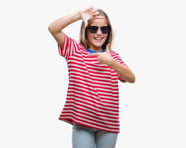 Genç güzel kız elle yapma çerçeve ve parmakları ile mutlu yüz gülümseyen izole arka plan üzerinde güneş gözlüğü takıyor. Yaratıcılık ve Fotoğrafçılık kavramı.