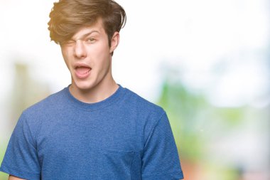 Seksi bir ifadeyle, neşeli ve mutlu yüzünü kameraya bakarak göz kırpıyor izole arka plan üzerinde mavi t-shirt giyen genç yakışıklı adam.