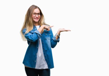 Genç güzel sarışın kadın hayrete ve el ile sunulması ve parmak ile işaret ederken kameraya gülümseyen izole arka plan üzerinde gözlük.