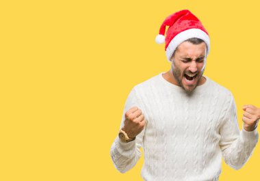 Gülümseyen ve başarı için çığlık izole arka plan çok mutlu ve heyecanlı kaldırdı, silah ile kazanan jest yapıyor üzerinde santa claus şapka giyen genç yakışıklı adam. Kutlama kavramı.