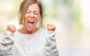 Üzerinde kış kazak giyen orta yaş üst düzey İspanyol kadın gülümseyerek ve başarı için çığlık arka plan çok mutlu ve heyecanlı kaldırdı, silah ile kazanan jest yapıyor izole. Kutlama kavramı.