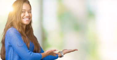 Açık el ile doğal gülümseyen girmek için davet izole arka plan üzerinde mavi kazak giyen genç güzel esmer kadın