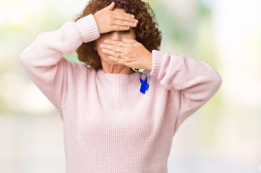 Değiştirilebilir mavi giyen orta ager üst düzey kadın şerit farkındalık izole arka plan üzerinde kaplama gözler renk ve şaşırttı ve şok ellerle ağız. Duygu gizleme