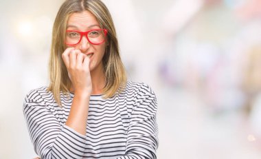 Stresli ve gergin elle çivi ısırma ağzına bakarak izole arka plan üzerinde gözlük takan genç güzel kadın. Anksiyete sorunu.