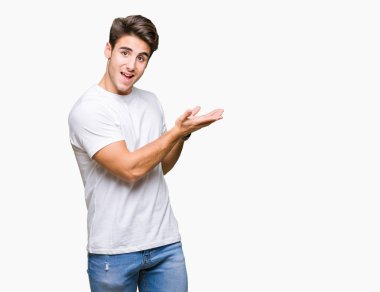 Arka plan üzerinde beyaz t-shirt giyen genç yakışıklı adam izole el ve reklam mutlu ve kendinden emin gülümseyen sunulması avuç, yanında işaret