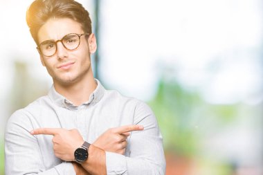 Genç yakışıklı adam gözlük izole üzerinde işaretleme için her iki parmak, farklı yönde ile katılmıyorum arka plan