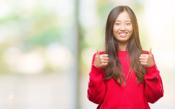 年轻的亚洲妇女穿着冬季毛衣在孤立的背景下成功标志做积极的手势与手 大拇指向上微笑和快乐 看着带着欢快表情的相机 胜利者的手势 — 图库照片