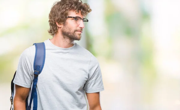 Handsome hispanic student man wearing backpack and glasses over isolated background looking away to side with smile on face, natural expression. Laughing confident.