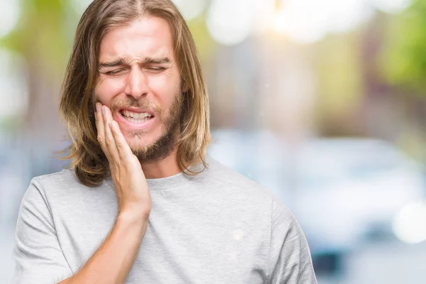 Young handsome man with long hair over isolated background touching mouth with hand with painful expression because of toothache or dental illness on teeth. Dentist concept.