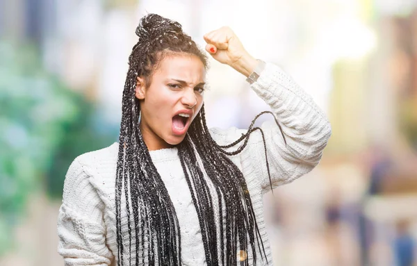 Young braided hair african american girl wearing sweater over isolated background angry and mad raising fist frustrated and furious while shouting with anger. Rage and aggressive concept.