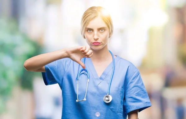 若い美しい金髪の医者の外科医看護師女性不幸なと怒って拒否反応を示さず ジェスチャーを親指で否定的な分離の背景の上 不適切な表現 — ストック写真