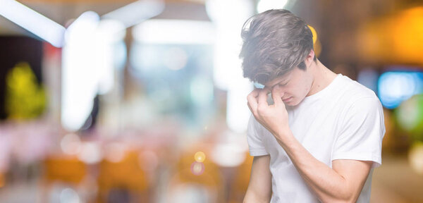 Young handsome man wearing casual white t-shirt over isolated background tired rubbing nose and eyes feeling fatigue and headache. Stress and frustration concept.