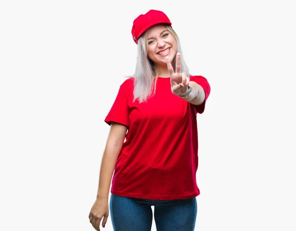 年轻的金发女人戴着红色的帽子在孤立的背景微笑着快乐的脸眨眼在相机做胜利的标志 第二个 — 图库照片