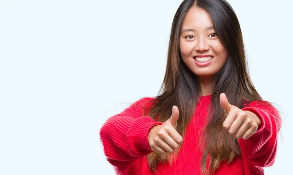 肯定的なジェスチャーをして承認する孤立した背景に冬のセーターを着ている若いアジア女性は親指笑顔と幸せな成功のためです カメラ 勝者のジェスチャーを見てください — ストック写真
