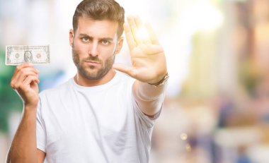 Açık eliyle dur işareti ile ciddi ve kendine güvenen ifade, savunma jest yapıyor izole arka plan üzerinde dolar tutan genç yakışıklı adam