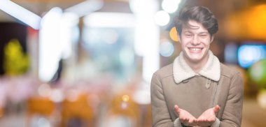 Genç yakışıklı adam giyen kış ceket izole üzerinden alma veya jest vererek birlikte el avuç içi ile gülen arka plan. Ayrı tutma ve koruma