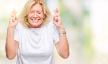 Orta yaş sarışın kadın geçiş parmakları umut ve gözler gülümseyen izole arka plan yüzünden kapalı. Şans ve batıl kavramı.