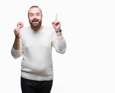 Genç beyaz hipster man yemek tatlı çörek üzerinde arka plan ile bir fikir ya da gülen yüz, bir numara ile parmak işaret soru sürpriz izole