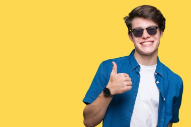 Genç yakışıklı adam hareketi el ile mutlu yaşasın yapıyor izole arka plan üzerinde güneş gözlüğü takıyor. Kameraya bakarak başarı gösteren ile ifade onaylama.