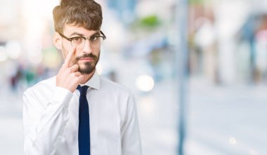Genç yakışıklı iş adam gözlük izole üzerinde arka plan işaret jest göz izlemek için şüpheli ifade