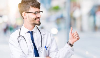 Yanına bir jest yapıyorsun gülümseyen hastane bir palto giyiyor gurur, seyir izole arka plan üzerinde genç doktor adam yaşasın