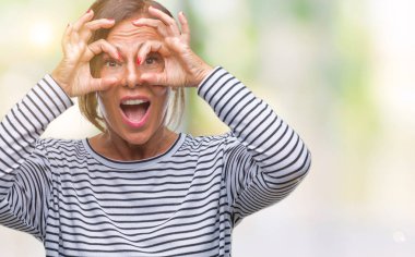 Orta yaş üst düzey İspanyol kadın dilini, parmaklarının arasından baktığını yapışmasını dürbün gibi ok jest yapıyor izole arka plan yüzünden. Deli ifade.