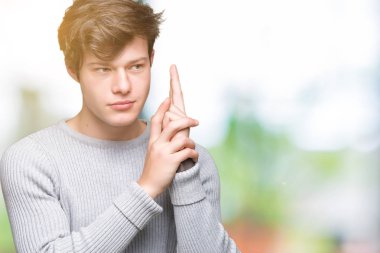 El hareketi ile sembolik silah tutan, çekim silah, kızgın yüz öldürmek oynamaya izole arka plan üzerinde kış kazak giyen genç yakışıklı adam