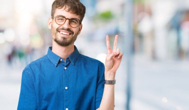 Mutlu yüz zafer işareti yaparken kameraya göz kırpıyor ile gülümseyen izole arka plan üzerinde gözlük takan yakışıklı delikanlı. İki numaralı.