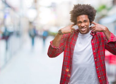 Yüksek sesle müzik gürültü rahatsız ifade parmaklarıyla kulaklarıyla kapsayan izole arka plan üzerinde Afro Amerikalı adam. Sağır kavramı.