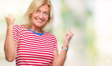 Gülümseyen ve başarı için çığlık orta yaş sarışın kadın izole arka plan çok mutlu ve heyecanlı kaldırdı, silah ile kazanan jest yapıyor. Kutlama kavramı.