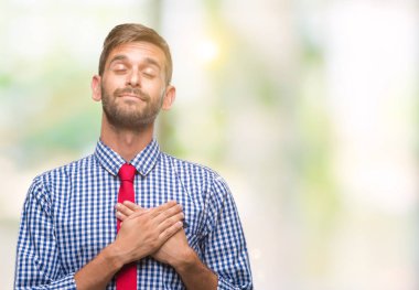 Genç yakışıklı iş adamı izole arka plan ile gülümseyen üzerinde kapalı gözler ve yüzünde minnettar jest ile göğüs üzerinde eller. Sağlık kavramı.