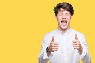 Genç yakışıklı iş adamı izole arka plan başarı işareti el ile pozitif jest yapıyor üzerinde başparmak gülümseyen ve mutlu. Neşeli bir ifadeyle, kazanan jest kameraya bakıyor.