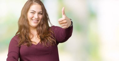 Güzel ve çekici artı boyutu izole arka plan onaylama üzerinde bir elbise giyen genç kadın başparmak gülümseyerek el ile pozitif jest yapıyor ve başarı için mutlu. Kamera, kazanan jest arıyorsunuz.